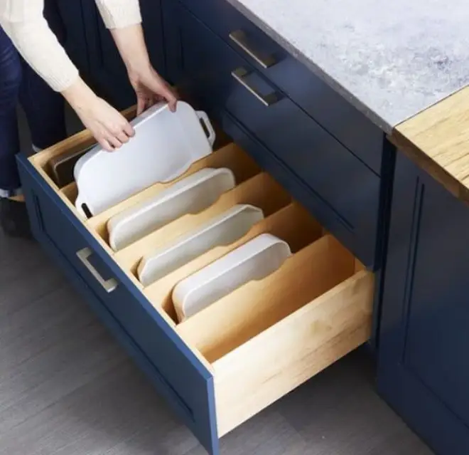 A pots and pans divider revealed in a lower kitchen cabinet, with a woman's hands pulling out a baking dish.