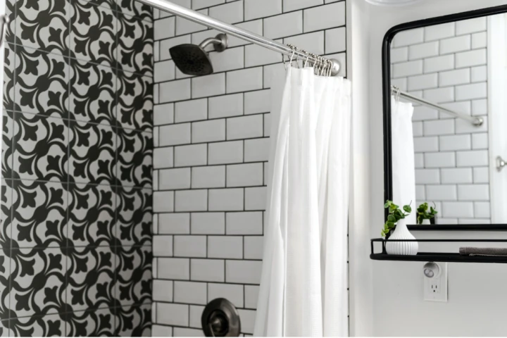 shower with one patterned black and white wall and one subway tiled wall with a white shower curtain