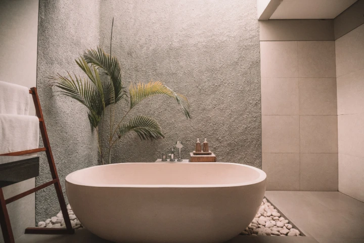elegant free standing bathtub with rough textured wall and large square tiles with fern in a plant pot for Small bathroom design ideas