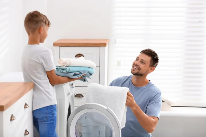 A person and child putting towels on a washing machine.