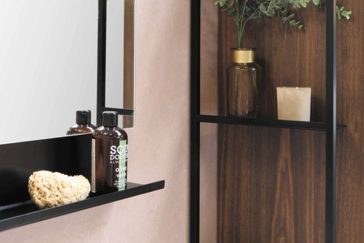 A shelf with a mirror and a candle and bottles on it.
