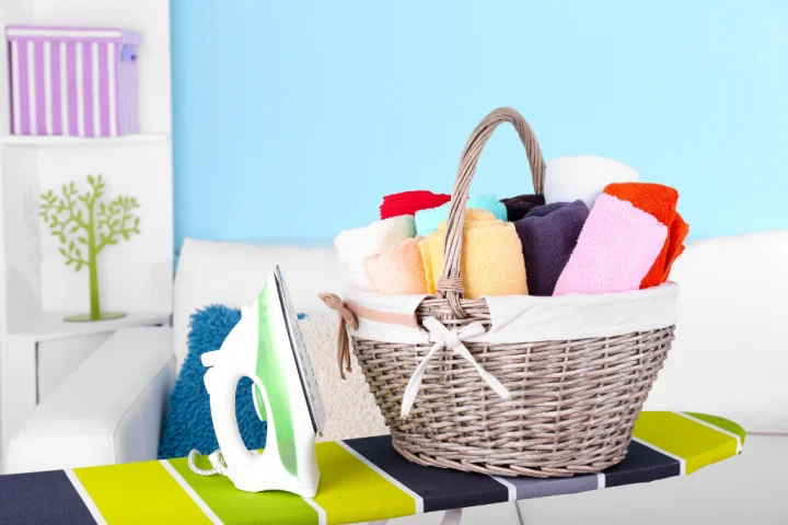 A basket full of towels and ironing board.