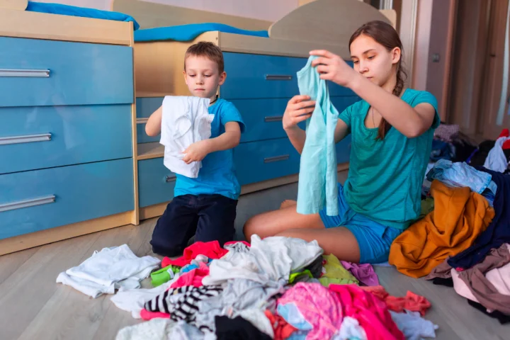 Children organize their clothes in front of custom-built beds with drawers.