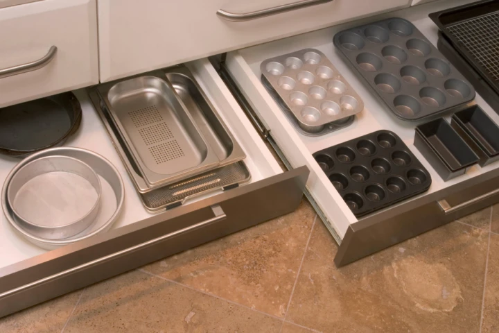 Baking pans and muffin tins stacked neatly on top of one another in a toe kick drawer.